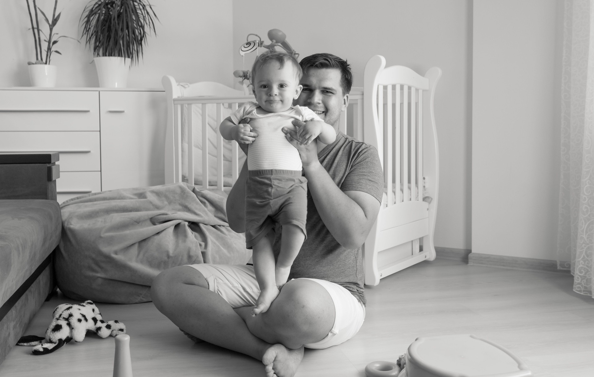 Monochrome image of father playing with baby at living room